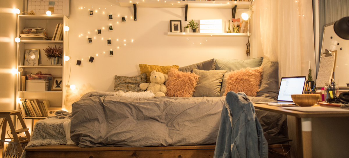 Ambassador by Maholi Inc's Feather & Down Duvet promotion featuring a cozy bedroom with grey bedding, layered pillows and warm string lights.