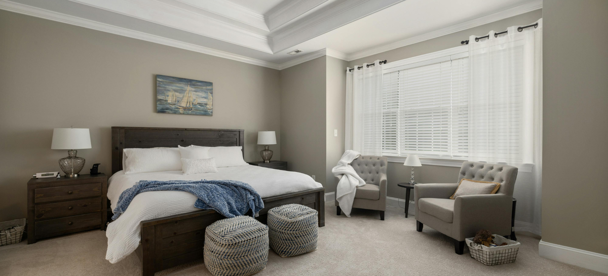 Bright, neutral-toned bedroom with white Royal Elite Hutterite goose down duvet by Maholi Inc. bedding, layered pillows and a textured blue throw on a dark wood bed.
