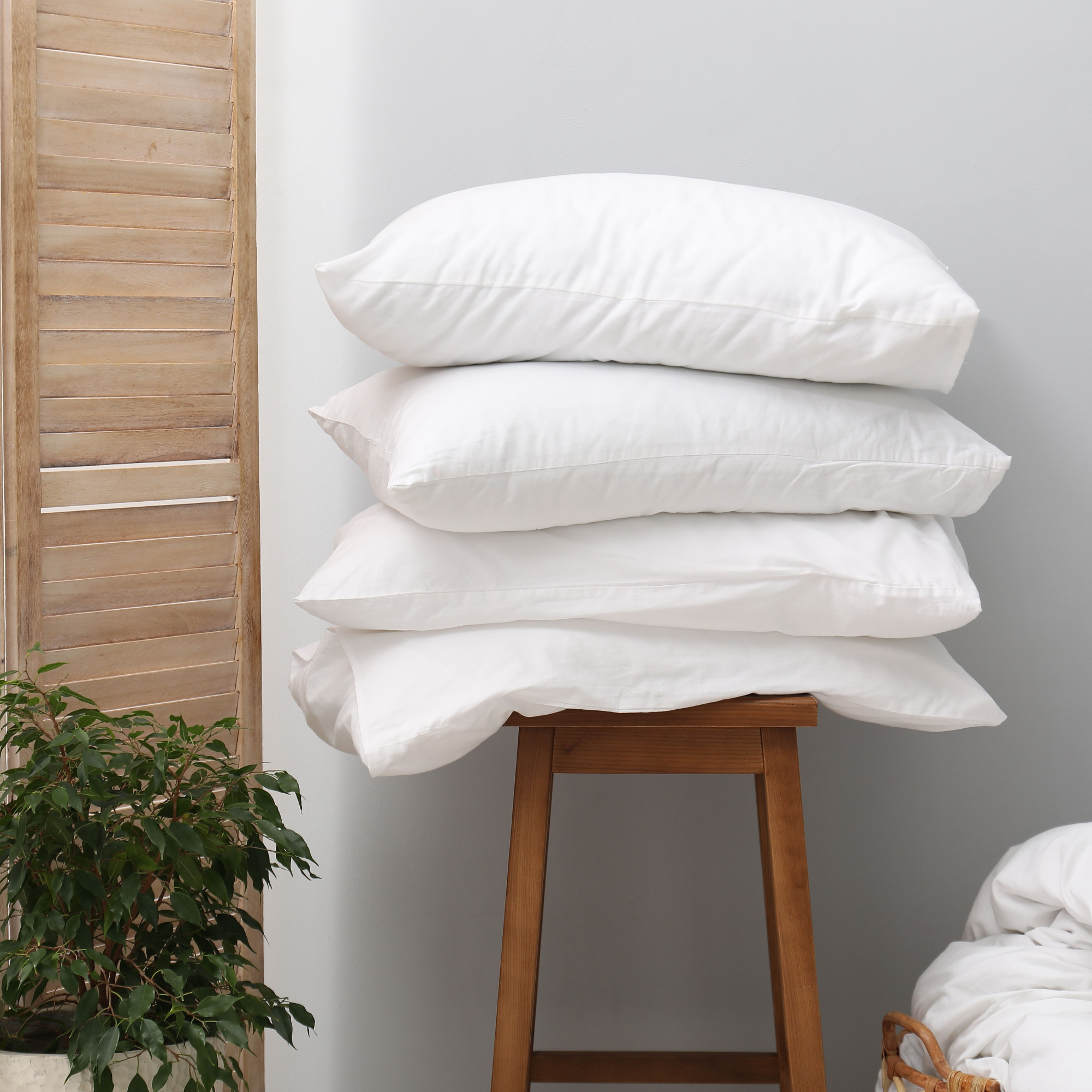Stack of white pillows on a wooden stool in a bedroom