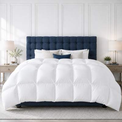 A neatly made bed in a bright bedroom setting, featuring a white fluffy Hutterute Goose Down comforter and matching white pillows with a navy blue tufted headboard and matching base.