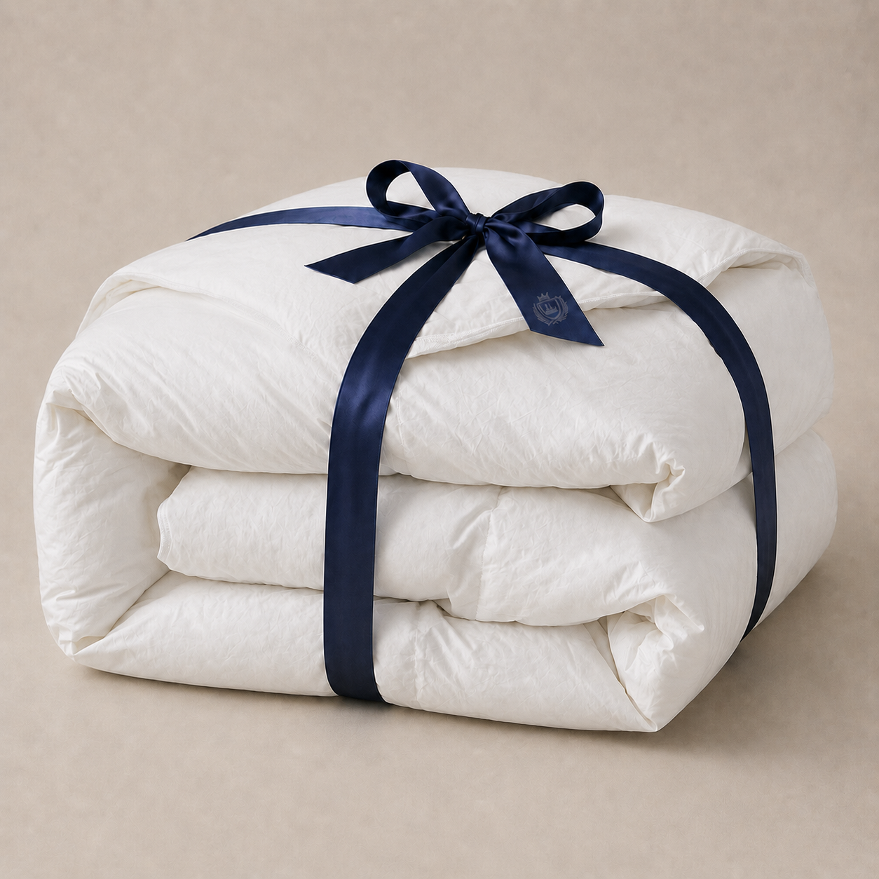 A folded fluffy 850 loft hutterite goose down comforter, wrapped with a dark navy blue satin ribbon tied in a bow, set against a neutral beige background. 