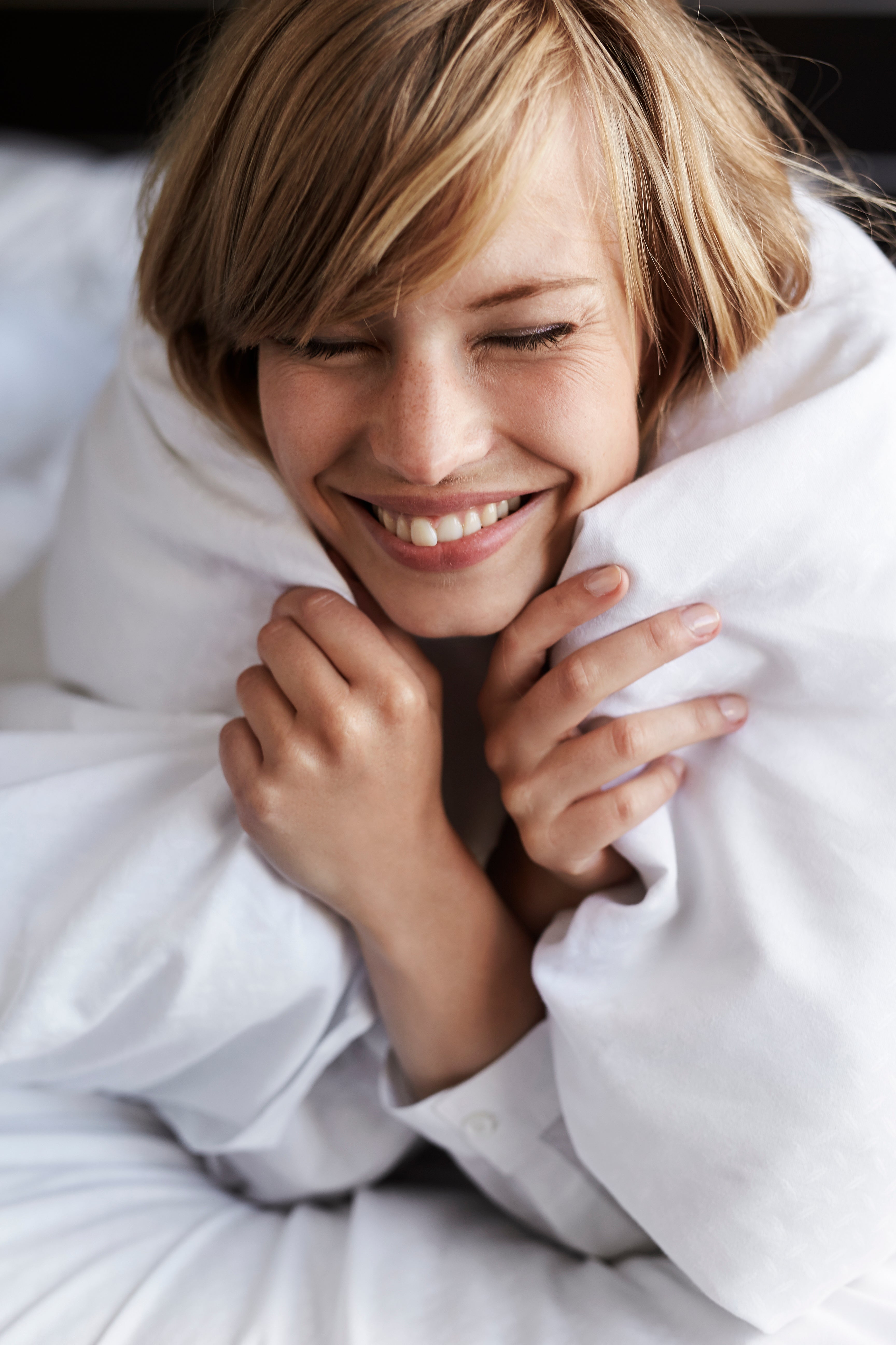 Woman resting with a Royal Elite best duvet comforter in a bright bedroom, representing soft comfort and premium bedding.
