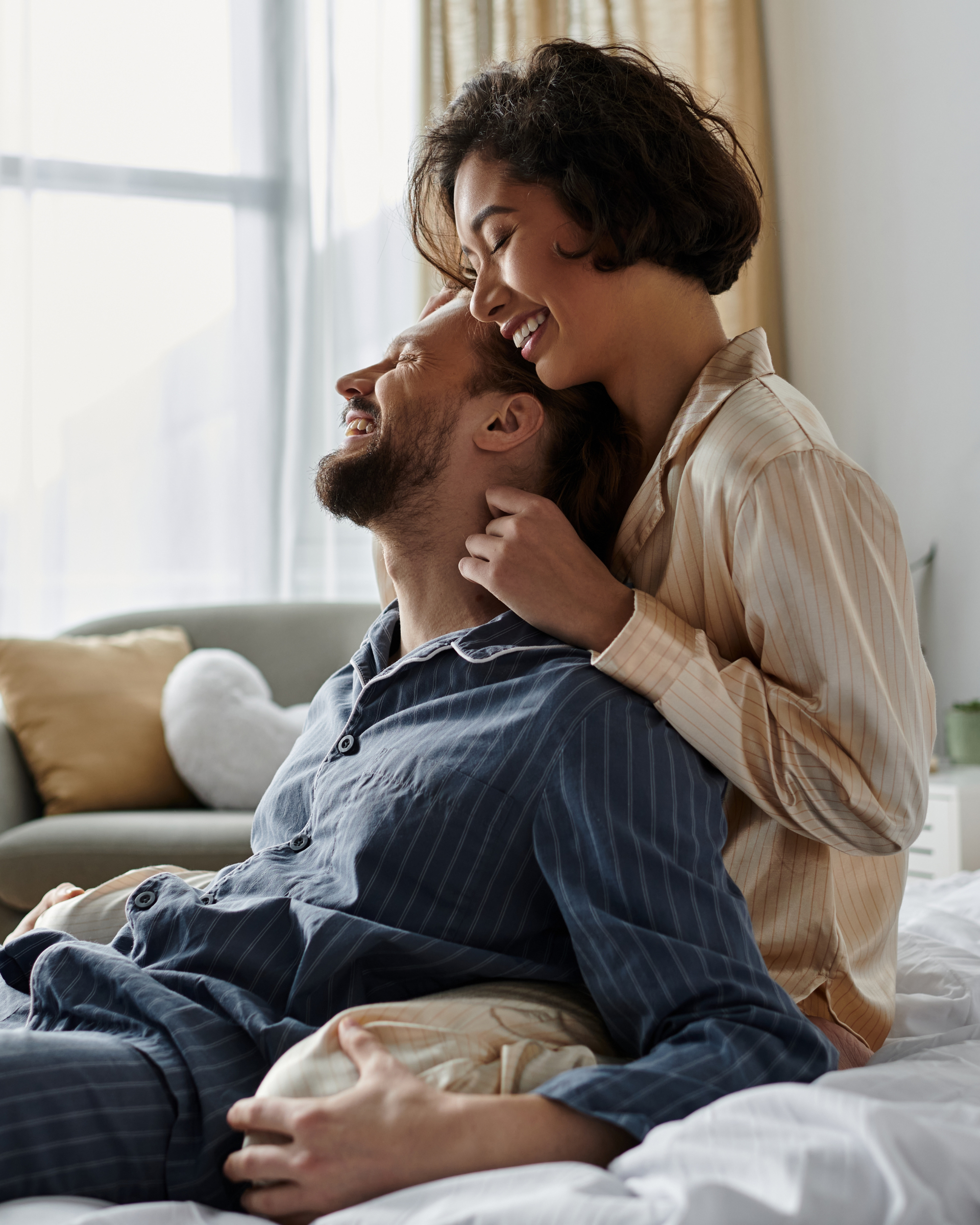 A smiling couple in matching pajamas sharing a tender moment on a Royal Elite bedding that is made in Canada of Canadian Hutterite White Duck Down 700 fill power in a softly lit bedroom. 