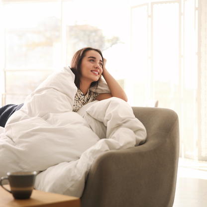 Woman wrapped in the Royal Elite Feather Duvet, enjoying its cozy comfort in a bright bedroom setting.