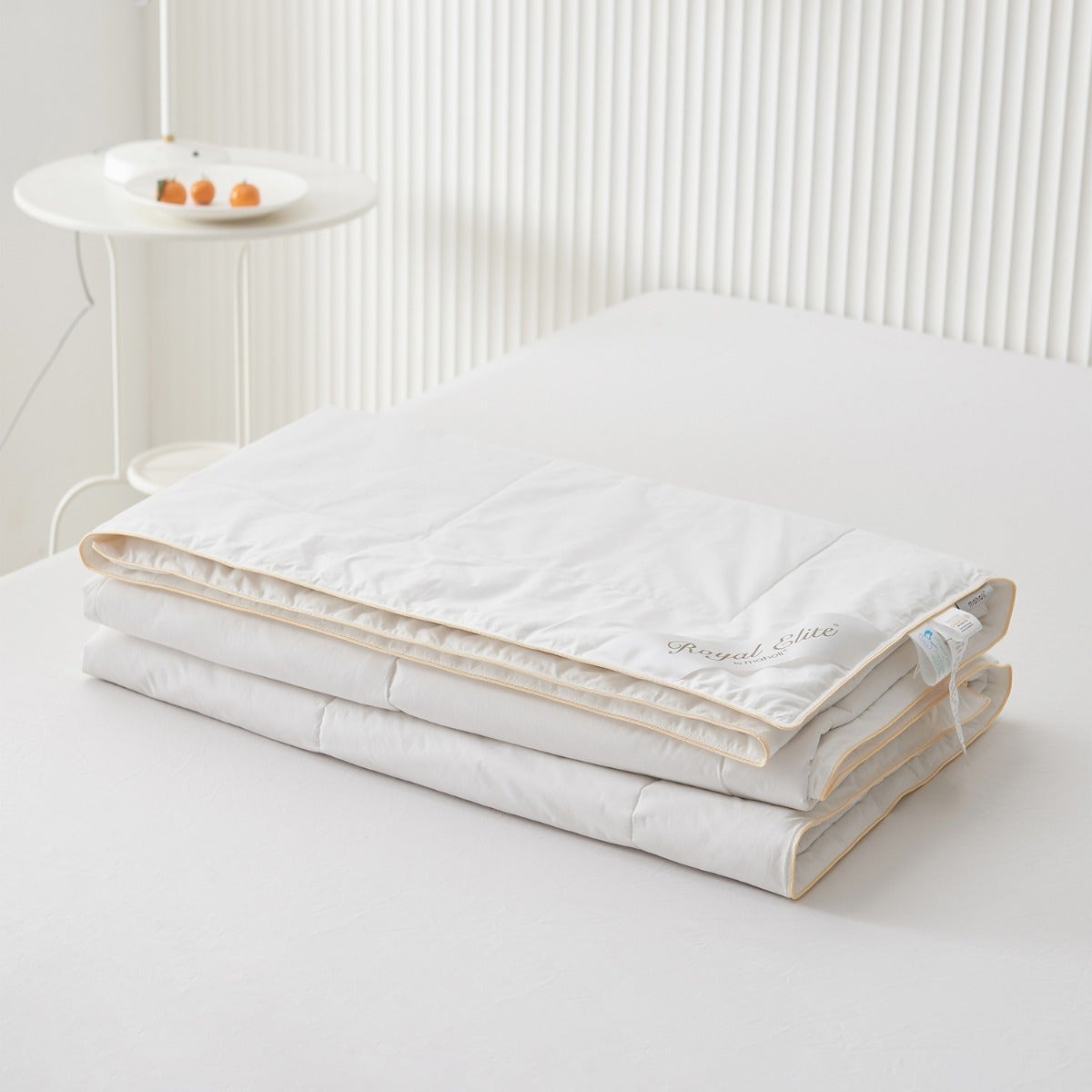 Royal Elite Silk Duvet folded on a bed, showing its low profile, gold piped edge and embroidered logo.