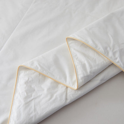 Corner of the Royal Elite Silk Duvet folded back, showing gold piped binding and the matte cotton percale shell.